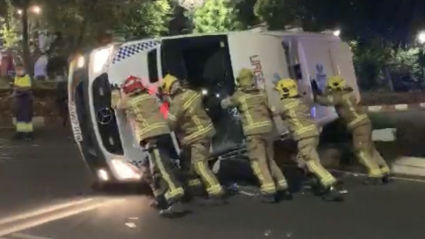 Bomberos empujando una ambulancia volcada tras un accidente