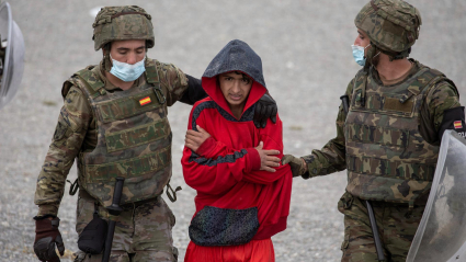 Soldados del ejército conducen a un joven en la playa ceutí de El Tarajal, hoy miércoles durante la masiva entrada de migrantes por la frontera que une la ciudad autónoma con Marruecos. 