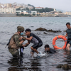 Un soldado del Ejército ayuda a dos migrantes a salir del agua en la playa de El Tarajal. La frontera entre España y Marruecos en la ciudad española de Ceuta