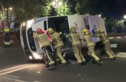 Bomberos empujando una ambulancia volcada tras un accidente