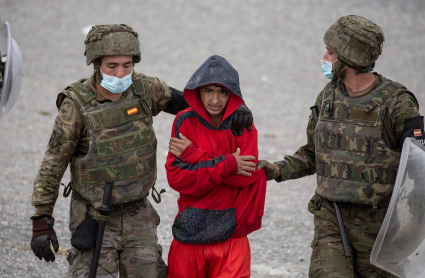 Soldados del ejército conducen a un joven en la playa ceutí de El Tarajal, hoy miércoles durante la masiva entrada de migrantes por la frontera que une la ciudad autónoma con Marruecos. 