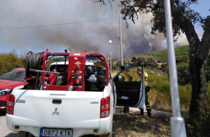 Un coche de bomberos frente a una columna de humo en el campo